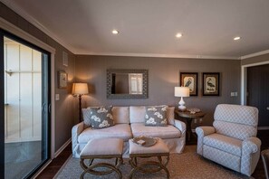 A living room with a sofa, ottoman, and chair, a small table, and two wall-mounted lamps. - Inlet Point Villas 1br/1b oceanfront w/pool 13D (North Myrtle Beach)