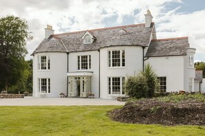 A large, white, two-story house with a grey roof, multiple windows, and a well-maintained lawn. - Moore Lodge (Ballymoney)