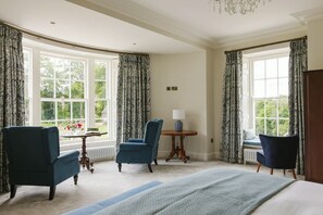 A hotel room with two blue armchairs, a small table with a lamp, and a bed with a blue bedspread. - Moore Lodge (Ballymoney)
