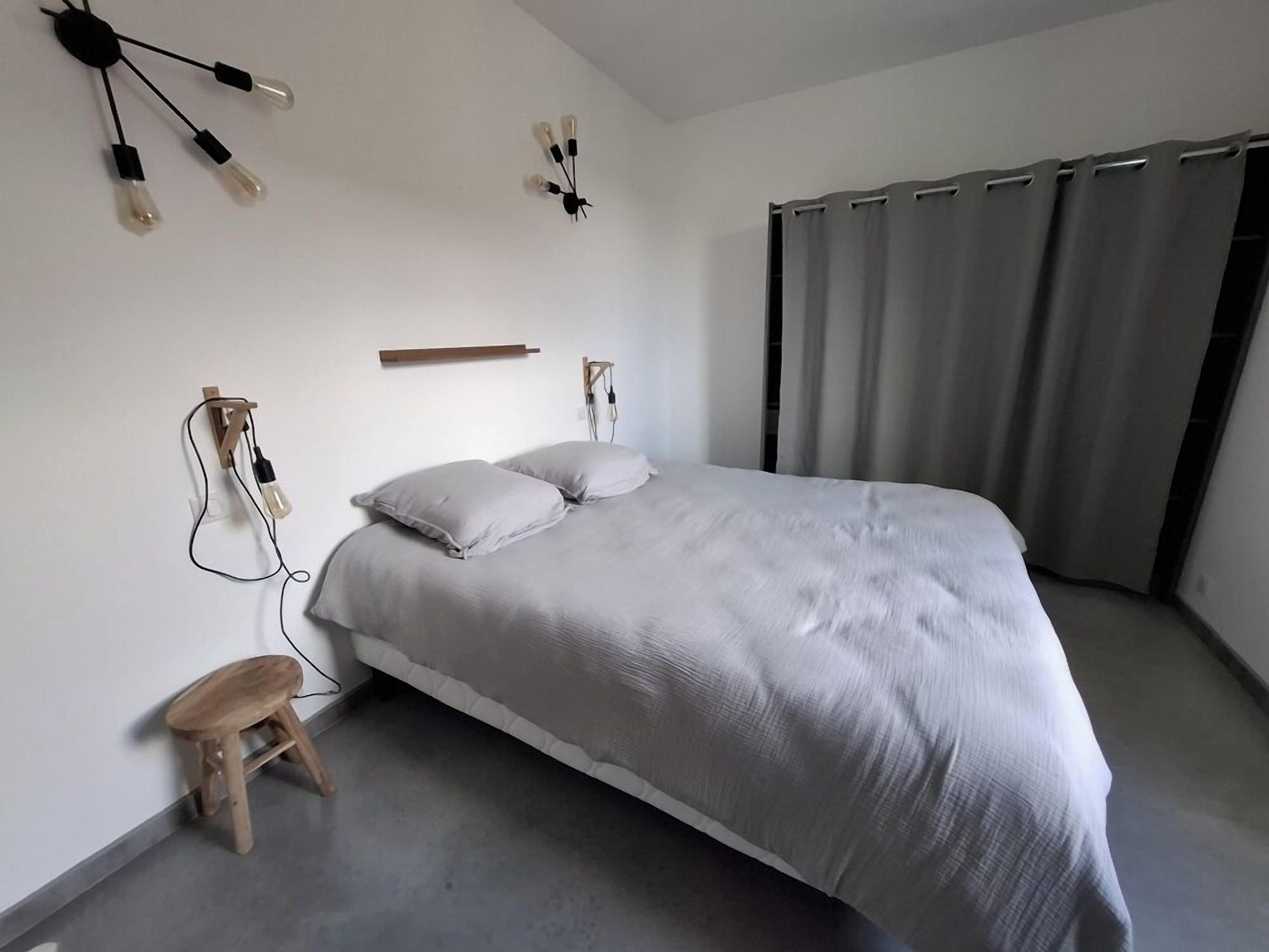 A bedroom with a bed, a wooden stool, and wall-mounted light fixtures.