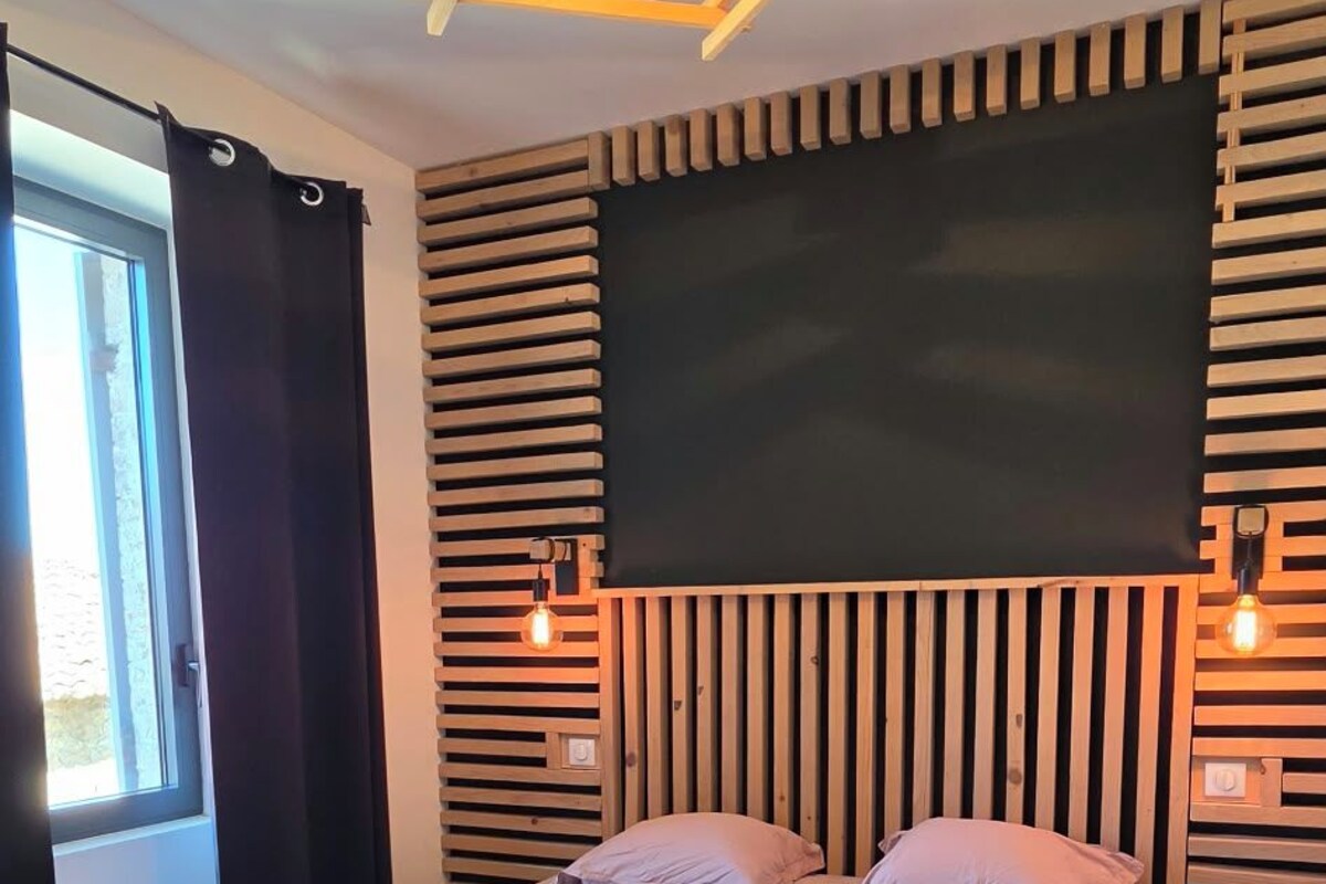 A modern bedroom with a large bed, wooden slat headboard, and a ceiling light fixture.