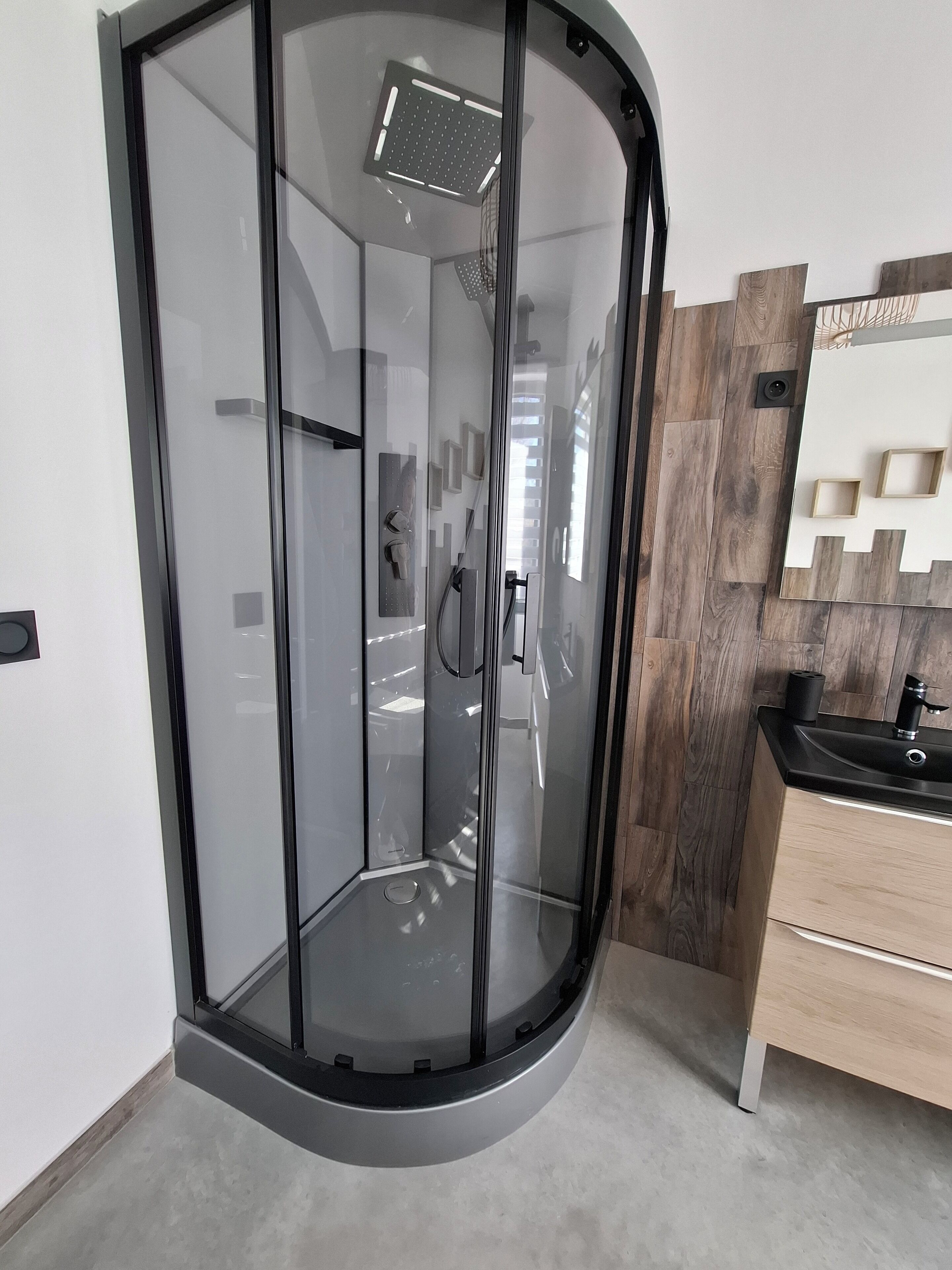 A modern bathroom with a glass-enclosed shower, a wooden vanity, and a mirror with a geometric design.