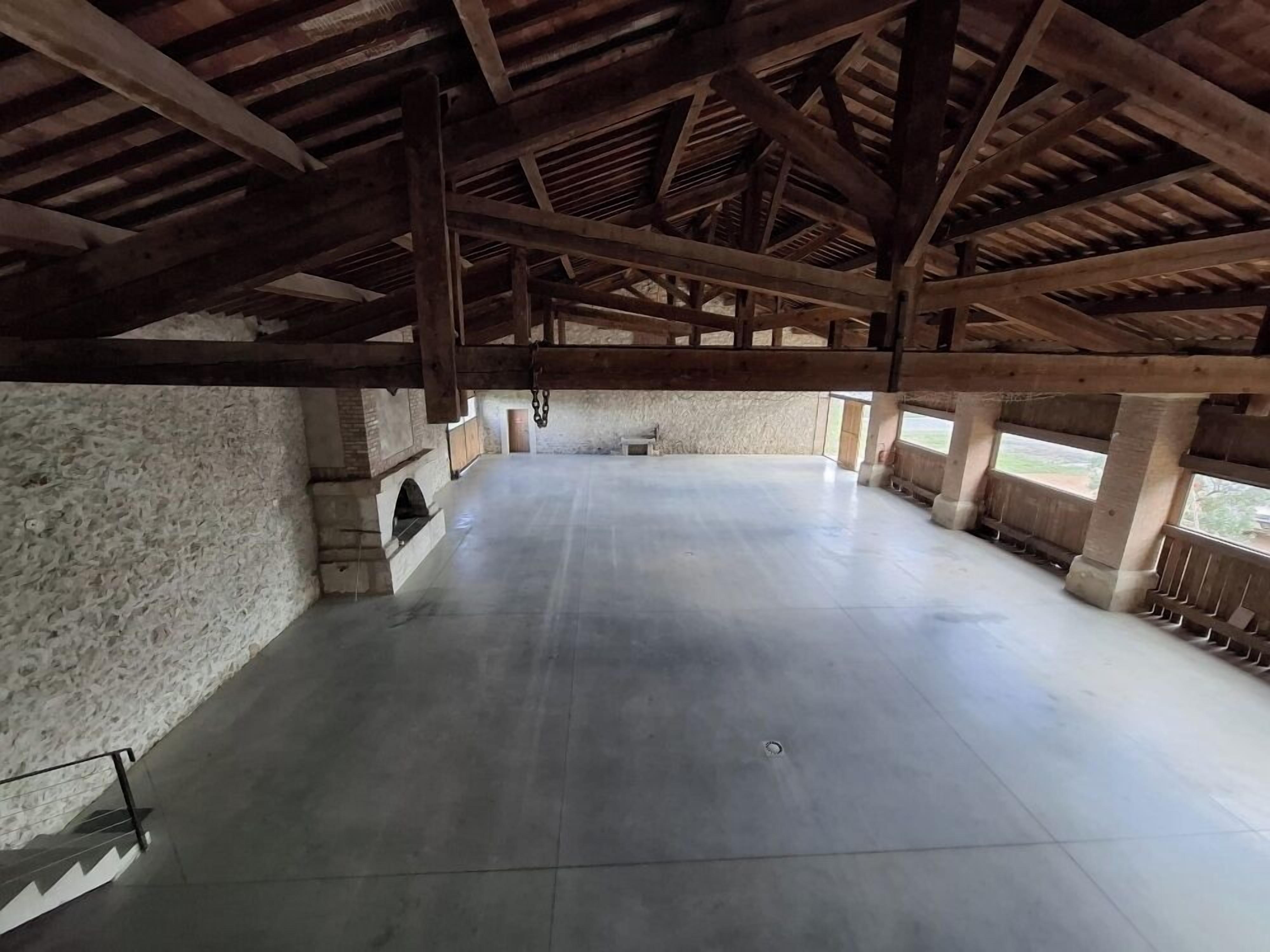 An interior with a high ceiling, exposed wooden beams, a large open space, stone walls, and a small window.