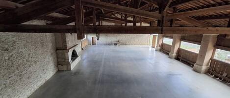 An interior with a high ceiling, exposed wooden beams, a large open space, stone walls, and a small window.