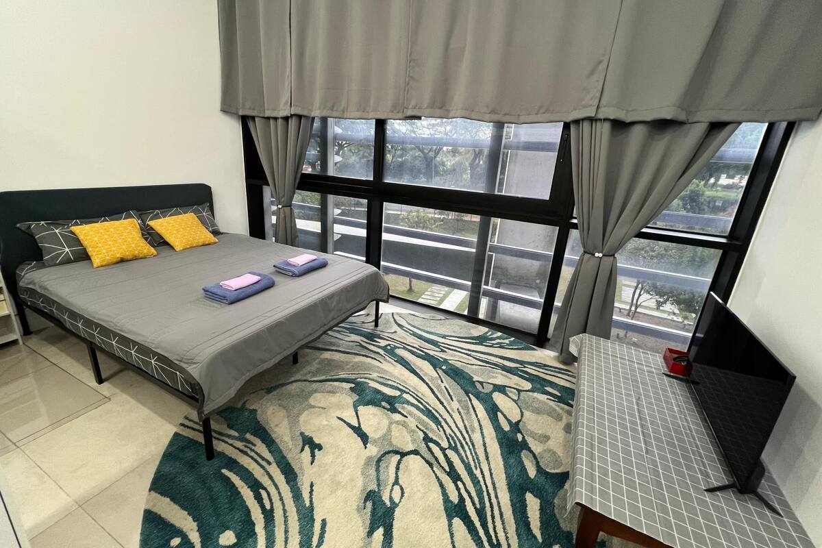 Un dormitorio con cama, escritorio, ventana con cortinas y vista a la calle.