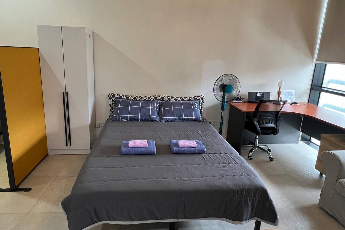 Un dormitorio con cama, escritorio, silla, ventilador y armario.