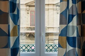 Una finestra con vista sulla facciata di un edificio e un balcone con ringhiera in metallo.