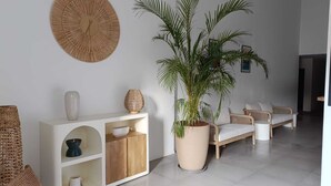 Een moderne woonkamer met een witte zithoek, een grote potplant en een witte console met decoratieve objecten.