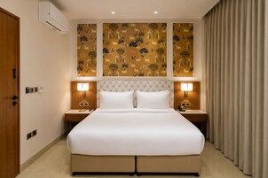 A hotel room with a large bed, two bedside tables, a headboard with a patterned design, and a wall-mounted air conditioning unit.