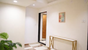 A hallway with a checkered floor, a wooden door, a mirror, and a framed picture on the wall. - Hotel Raw Leaves Premium Family & Business Hotel Near Rajkot Railway Station (Rajkot)
