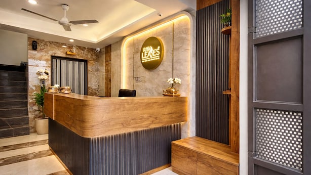A reception desk with a wooden finish and a circular logo above it. - Hotel Raw Leaves Premium Family & Business Hotel Near Rajkot Railway Station (Rajkot)