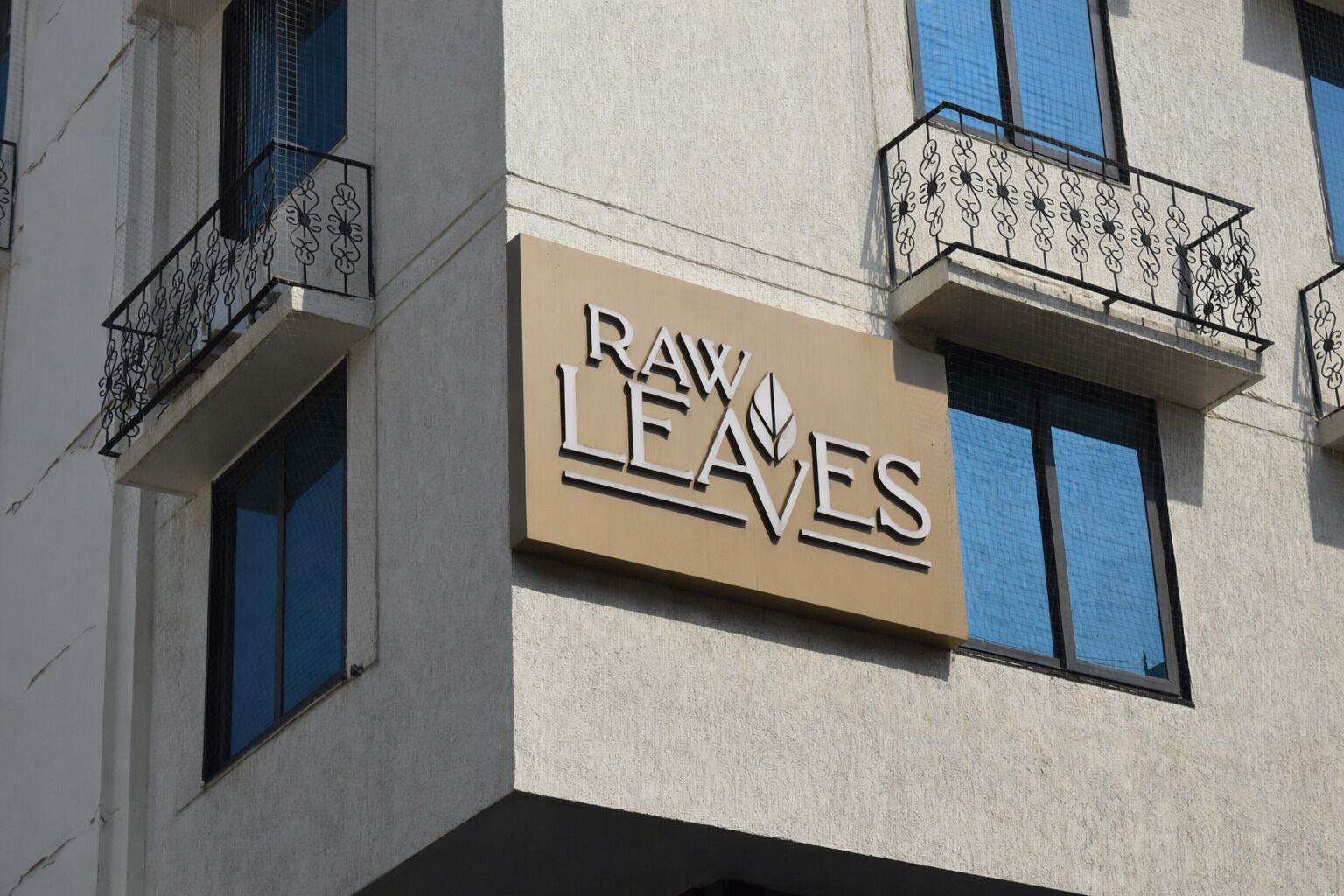 A building with a sign reading "Raw Leaves" and balconies with decorative railings.