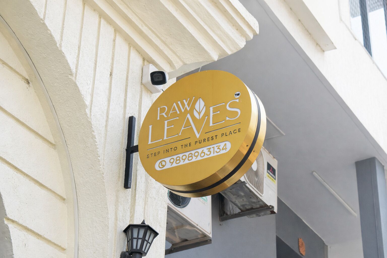 A gold sign with the text "Raw Leaves" and a phone number, mounted on a building.