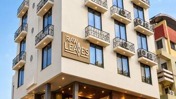 Un hotel de varios pisos con balcones, un letrero que dice 'RAW LEAVES' y un diseño arquitectónico moderno.