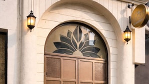 A large, ornate metal door with a decorative glass panel above it, flanked by two wall-mounted lanterns. - Hotel Raw Leaves Premium Family & Business Hotel Near Rajkot Railway Station (Rajkot)