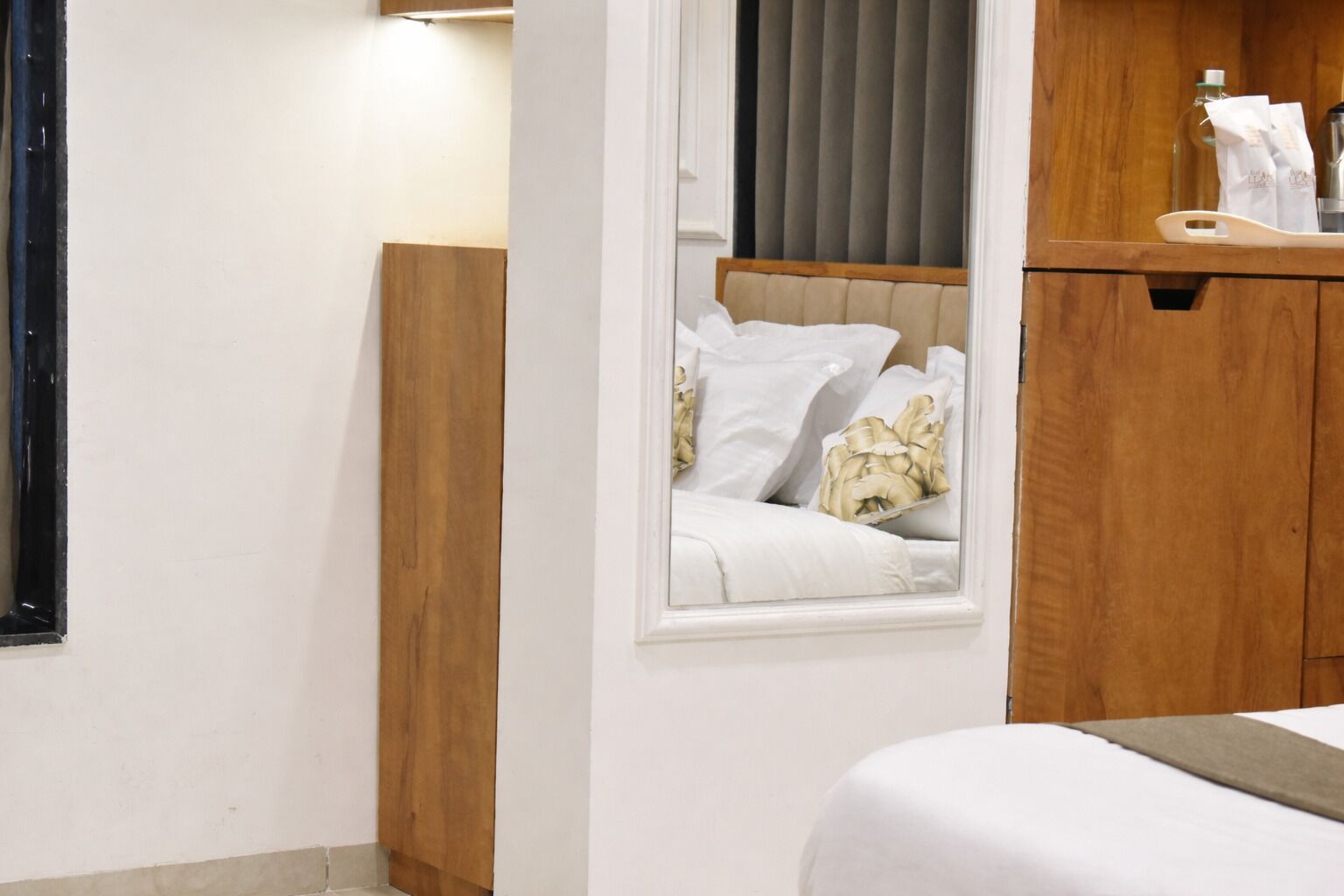 A hotel room with a bed, a wooden headboard, a window with curtains, and a wooden cabinet with toiletries.