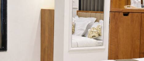 A hotel room with a bed, a wooden headboard, a window with curtains, and a wooden cabinet with toiletries.