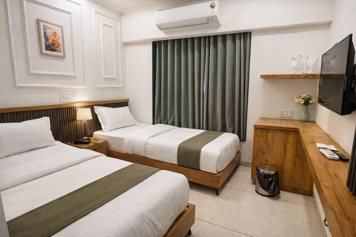 Une chambre d’hôtel avec deux lits, une tête de lit en bois, un petit bureau en bois, une poubelle, un téléviseur et un tableau au mur.