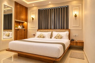 Quarto de hotel moderno com uma cama grande, cabeceira de madeira, mesas de cabeceira, um espelho e iluminação embutida na parede.