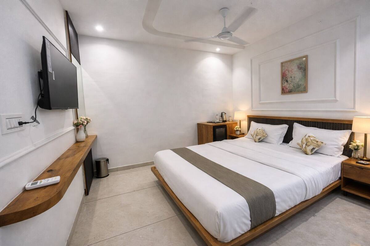 Une chambre d’hôtel moderne avec un grand lit, un téléviseur fixé au mur, une table de chevet en bois, une petite table et un ventilateur de plafond.