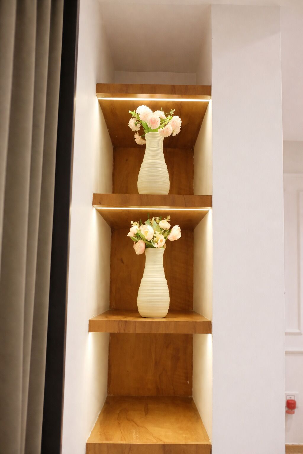 A staircase with two wooden shelves, each holding a white vase with flowers.