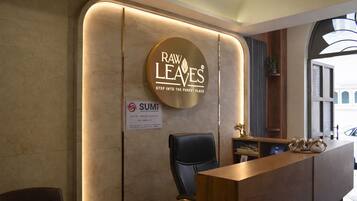 Ein Empfangsbereich mit einem Holztisch, einem schwarzen Bürostuhl und einem runden Schild mit dem Branding 'Raw Leaves'. Auch ein Schild mit 'SUMI' ist sichtbar.