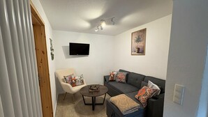 Ett vardagsrum med en soffa, en fåtölj och ett soffbord, en platt-TV och en tavla på väggen.