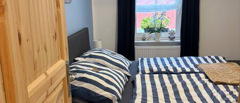 Un dormitorio con cama, ventana con cortinas, radiador y armario de madera.