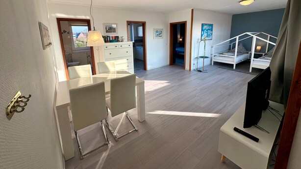 Ein großzügiger Wohnbereich mit Esstisch, Stühlen, einem Fernseher und einer Treppe, die zu einem Schlafzimmer führt.