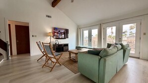 A spacious living room with a green sofa, wooden flooring, a ceiling fan, and a television mounted on the wall. - Spacious - Retama Retreat - Steps from Beach! (South Padre Island)