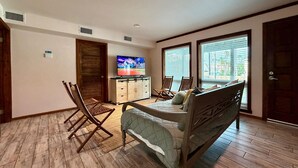 A spacious room with a bed, a TV, a wooden floor, and a view through large windows. - Spacious - Retama Retreat - Steps from Beach! (South Padre Island)