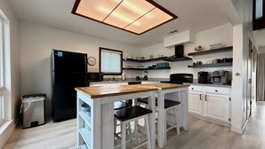 A modern kitchen with a central island, white cabinetry, and a black stove. - Spacious - Retama Retreat - Steps from Beach! (South Padre Island)