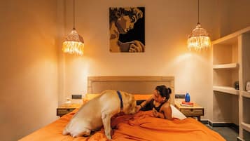 Un dormitorio con cama, un perro, un cuadro en la pared y dos lámparas colgantes.