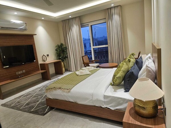 Een moderne hotelkamer met een groot bed, een flatscreen televisie aan de muur, een klein tafeltje en uitzicht op de stad.