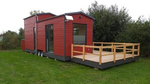 Une petite maison mobile rouge avec une terrasse en bois et une rampe d’accès.