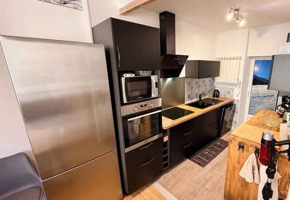 A modern kitchen with a stainless steel refrigerator, double ovens, a microwave, and a wooden countertop. - Les Soldanelles Le Mont Dore 12 pers (Mont-Dore)