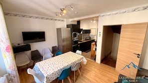 A compact living space with a dining area, kitchenette, and a small TV mounted on the wall. - Les Soldanelles, Le Mont Dore (sleeps 10) (Mont-Dore)