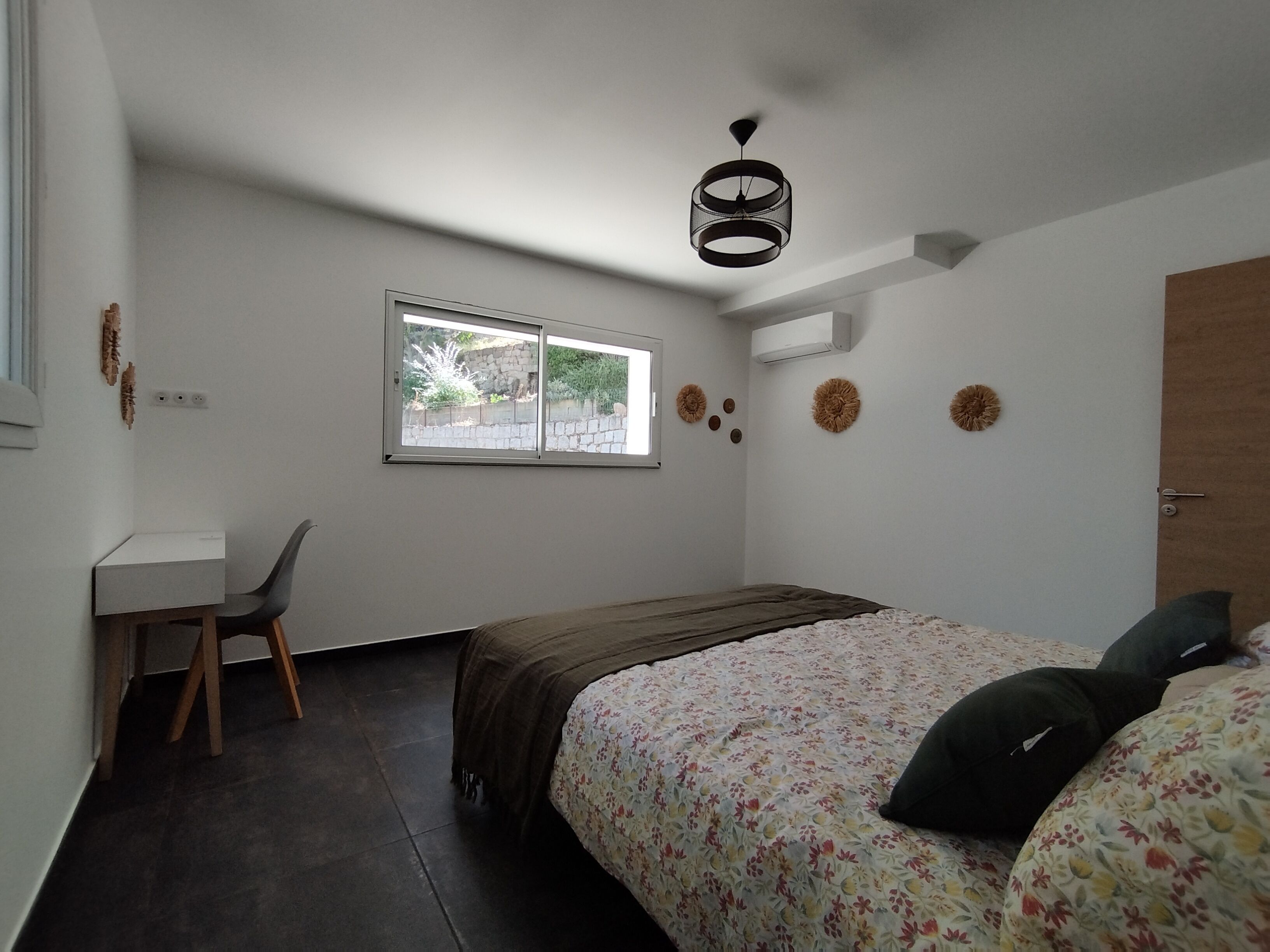 A small, well-lit bedroom with a single bed, a desk, and a window.