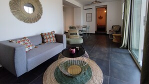 Un salón moderno con un sofá gris, cojines estampados, una mesa redonda de centro y un espejo grande en la pared.