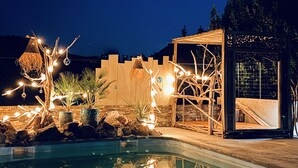 A pool with decorative lighting and plants, a wooden pergola, and a stone wall. - LA MAISON BRUNO DI SALVIO (Les Vans)