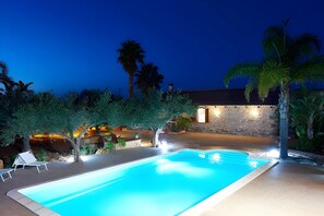 A swimming pool with a stone wall and palm trees in the background. - Villa Le Sterlizie con Piscina Privata (Castellammare del Golfo)