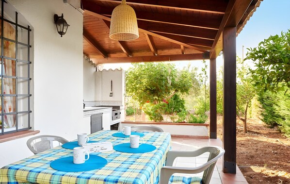Um pátio externo com uma mesa posta para dois, um lustre pendurado e vista para o jardim.