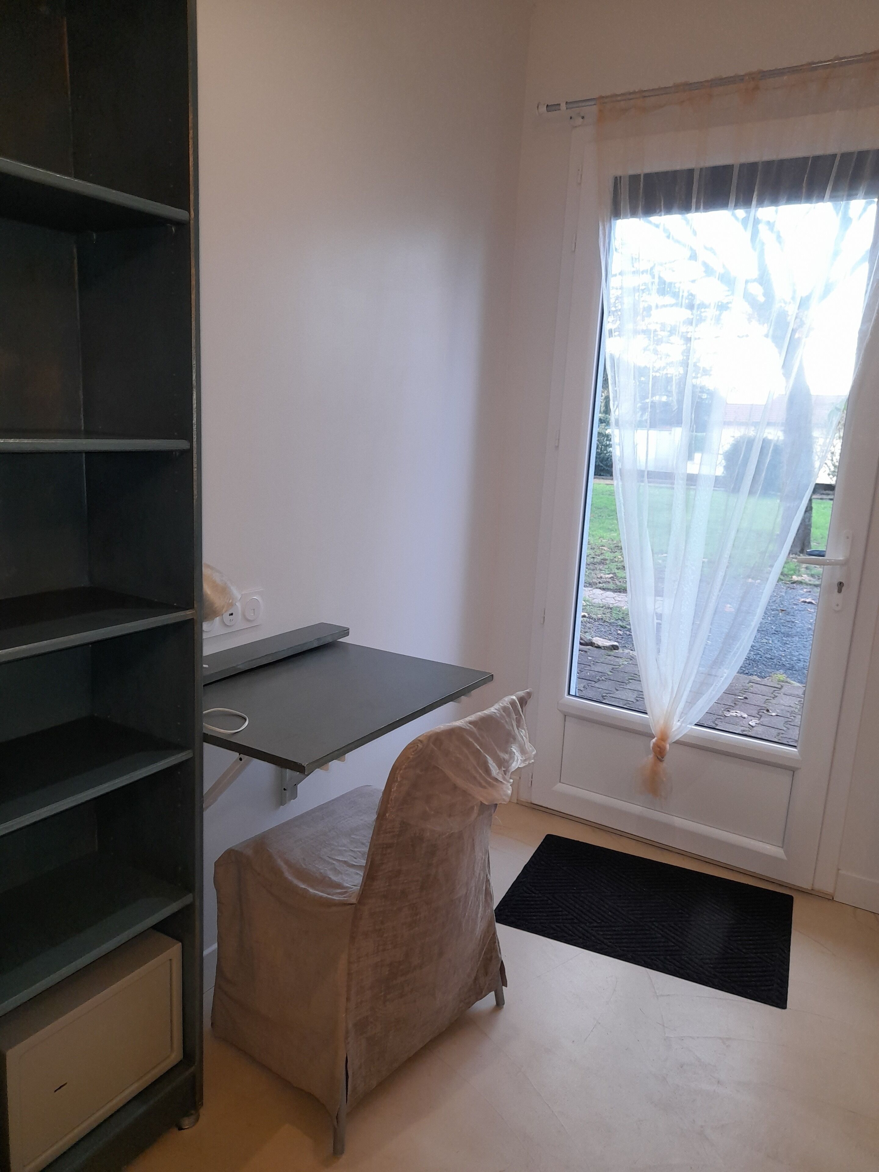 A room with a desk, a chair, and a window with sheer curtains.