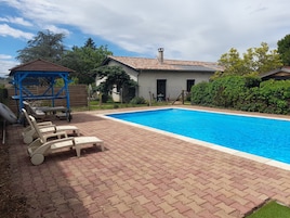 Una piscina con patio de ladrillo, sillas de descanso y un pabellón.
