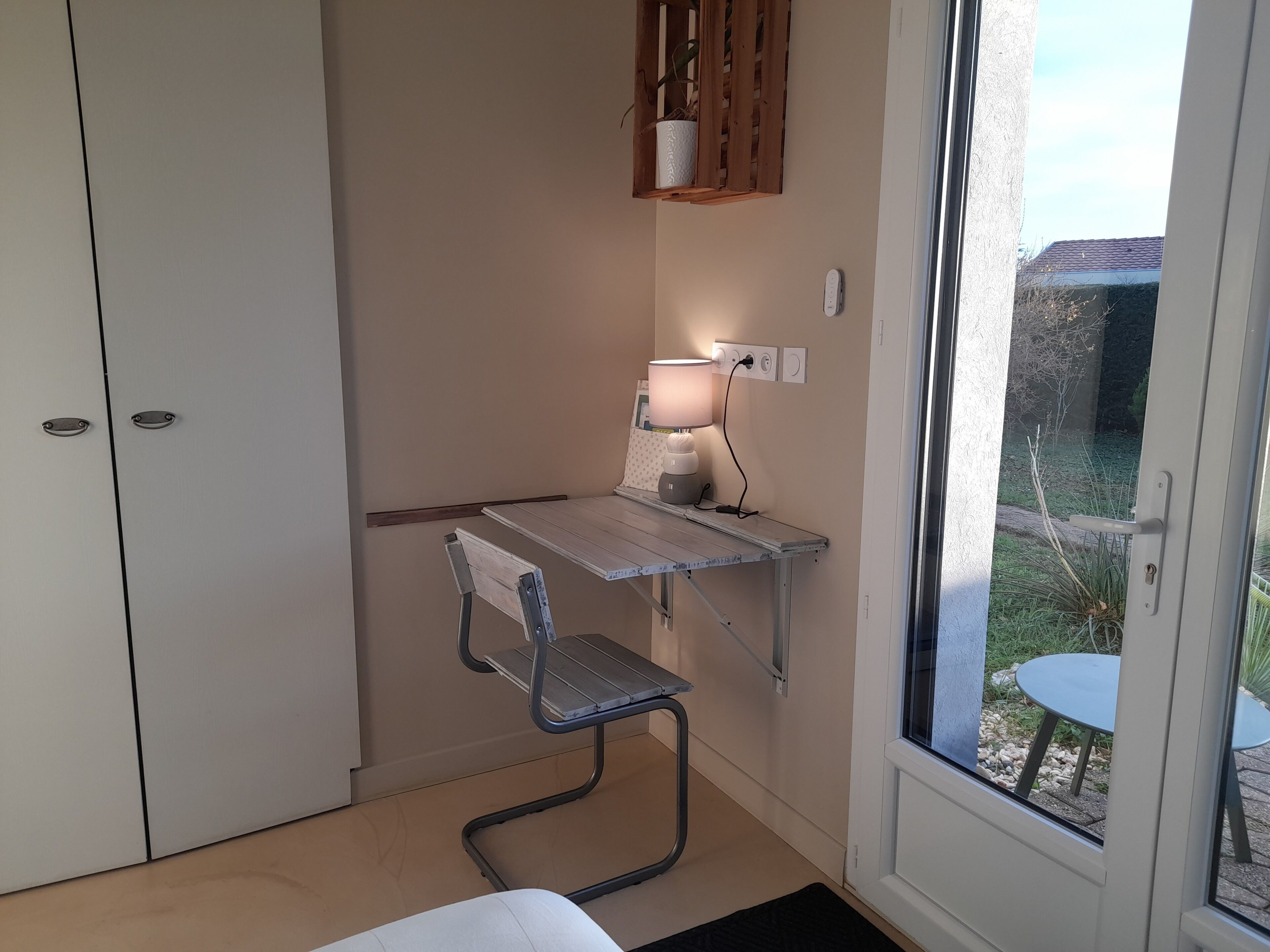 Una habitación pequeña y funcional con escritorio, silla y lámpara. Hay una ventana con vistas al exterior.