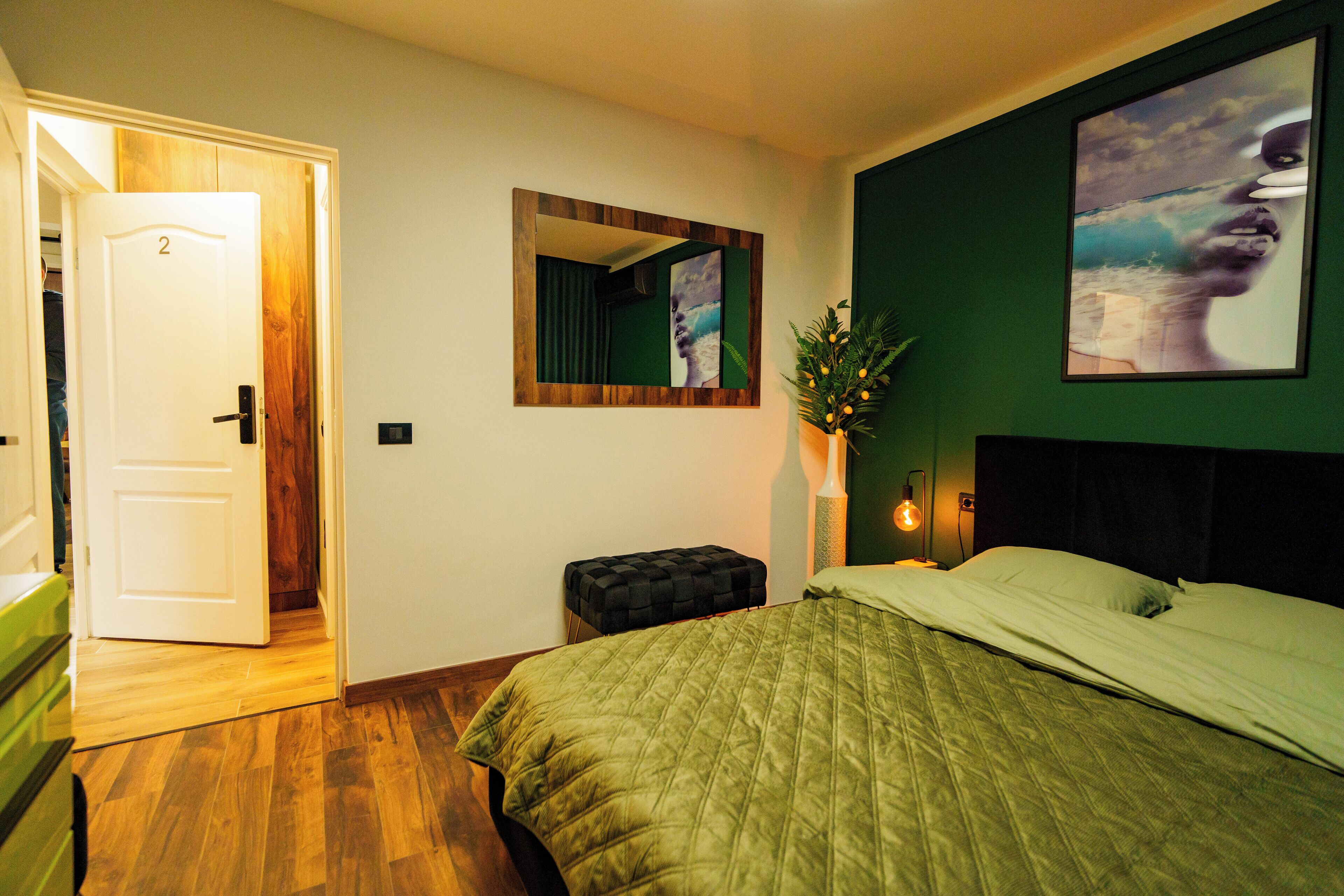 A bedroom with a bed, a nightstand, a mirror, and a door leading to another room.