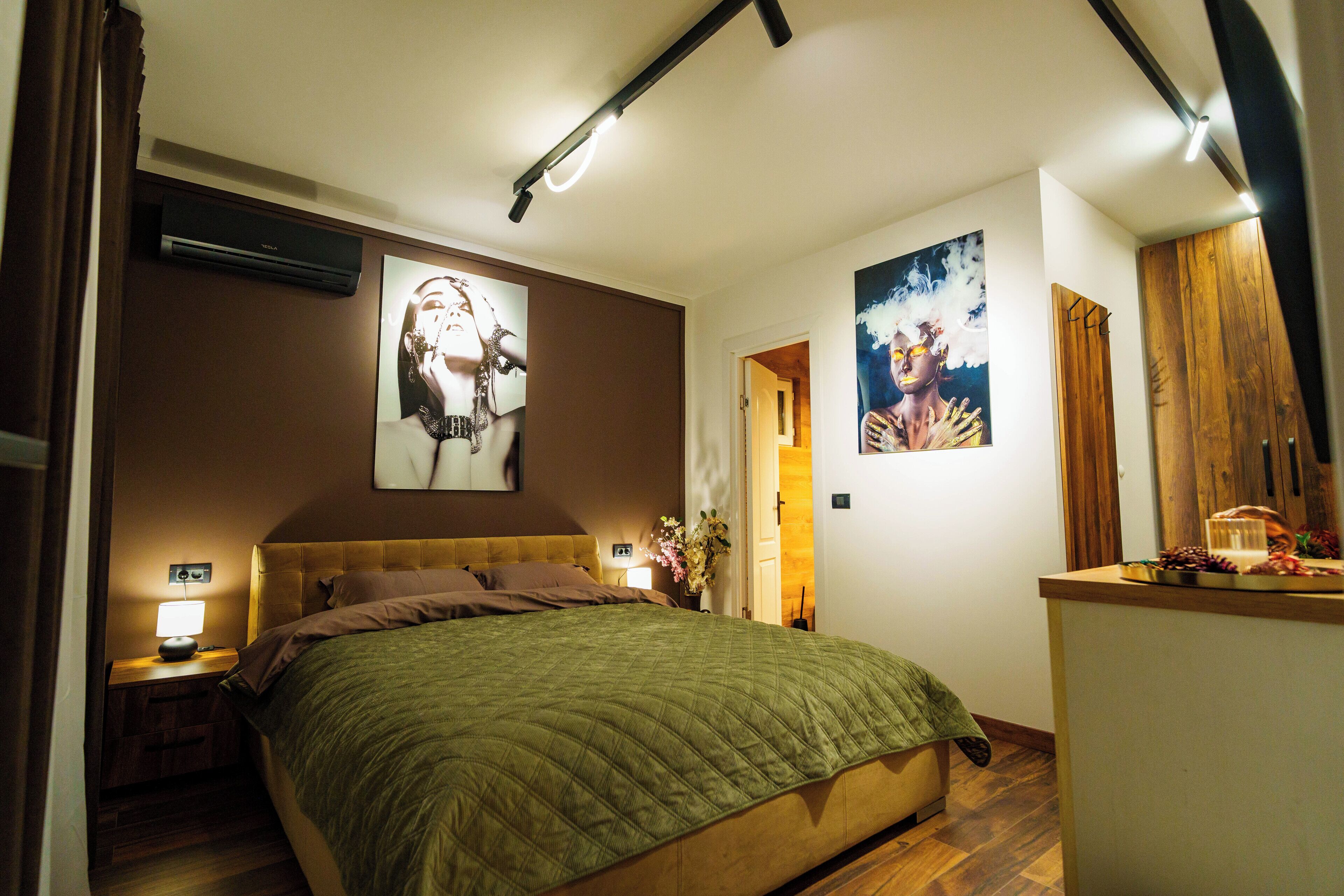Een slaapkamer met een bed, nachtkastjes, een wandairconditioner en kunstwerken.