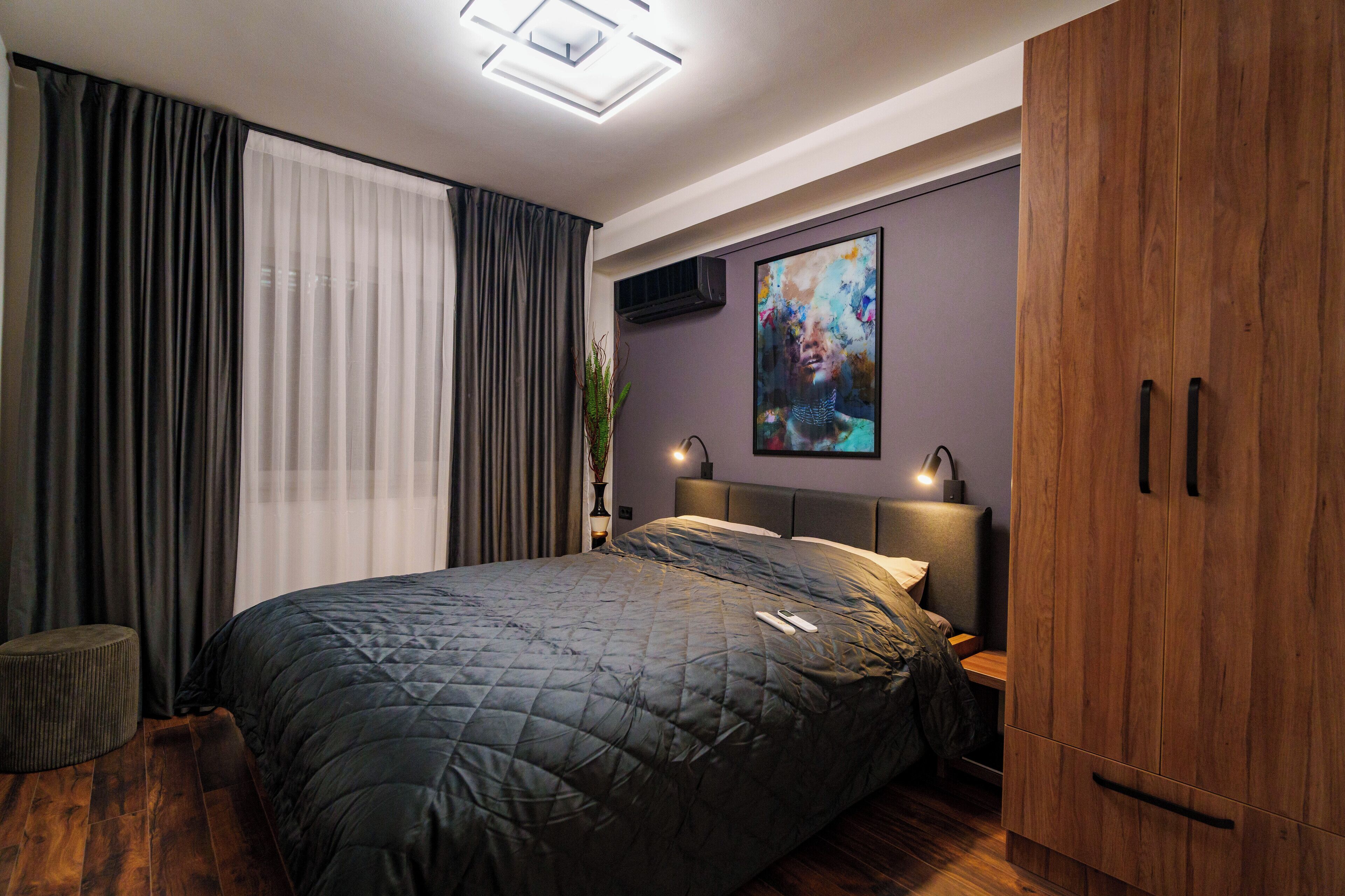 A modern bedroom with a large bed, a wooden wardrobe, and a painting on the wall.