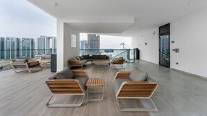 Un balcón espacioso con mobiliario moderno, vistas del horizonte urbano y barandilla de vidrio.