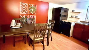 Un comedor con una mesa y sillas de madera, una cocina con refrigerador negro y gabinetes blancos, y decoración mural.
